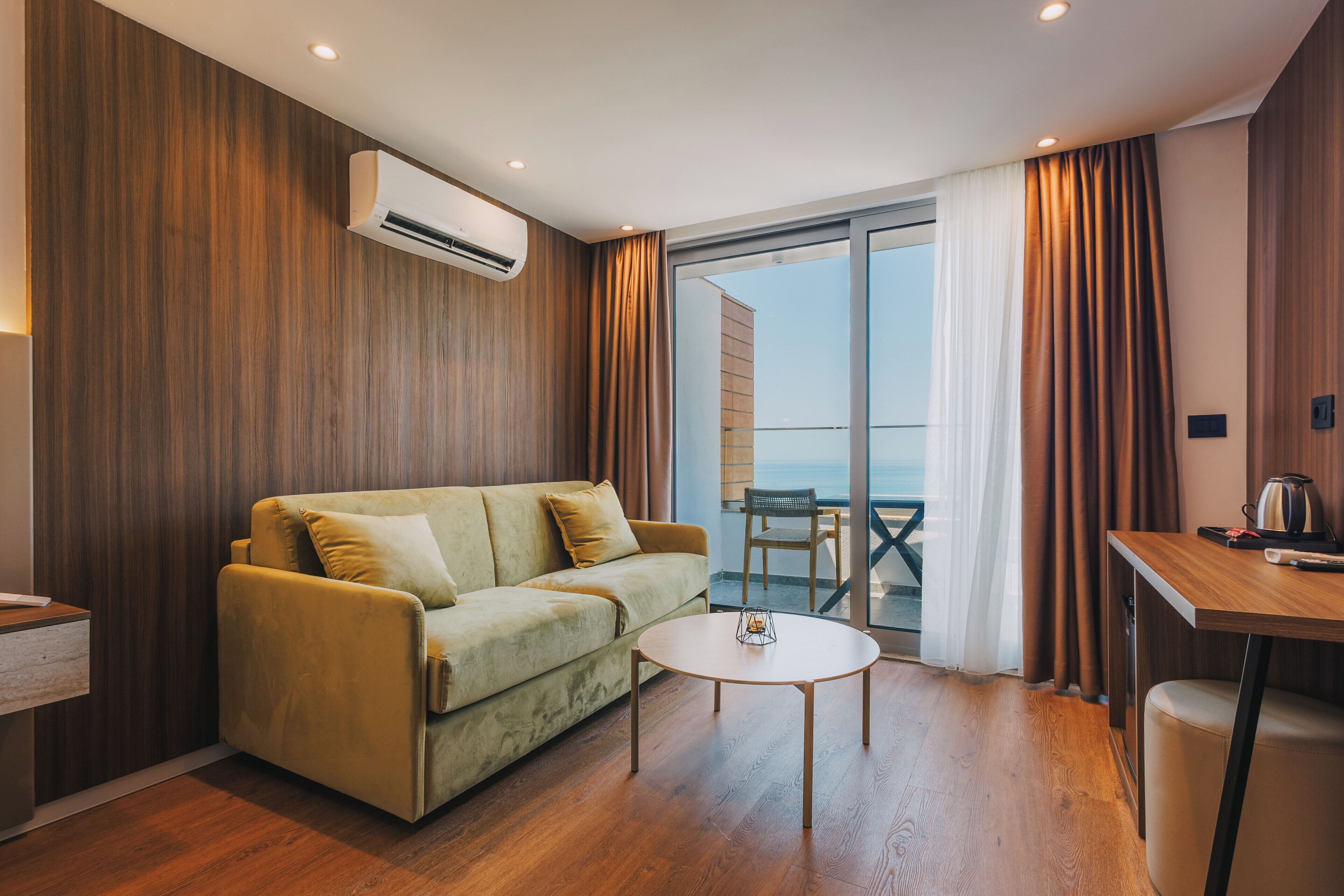 Un salon moderne avec un canapé, une petite table et une vue sur la mer, visible à travers une porte vitrée.