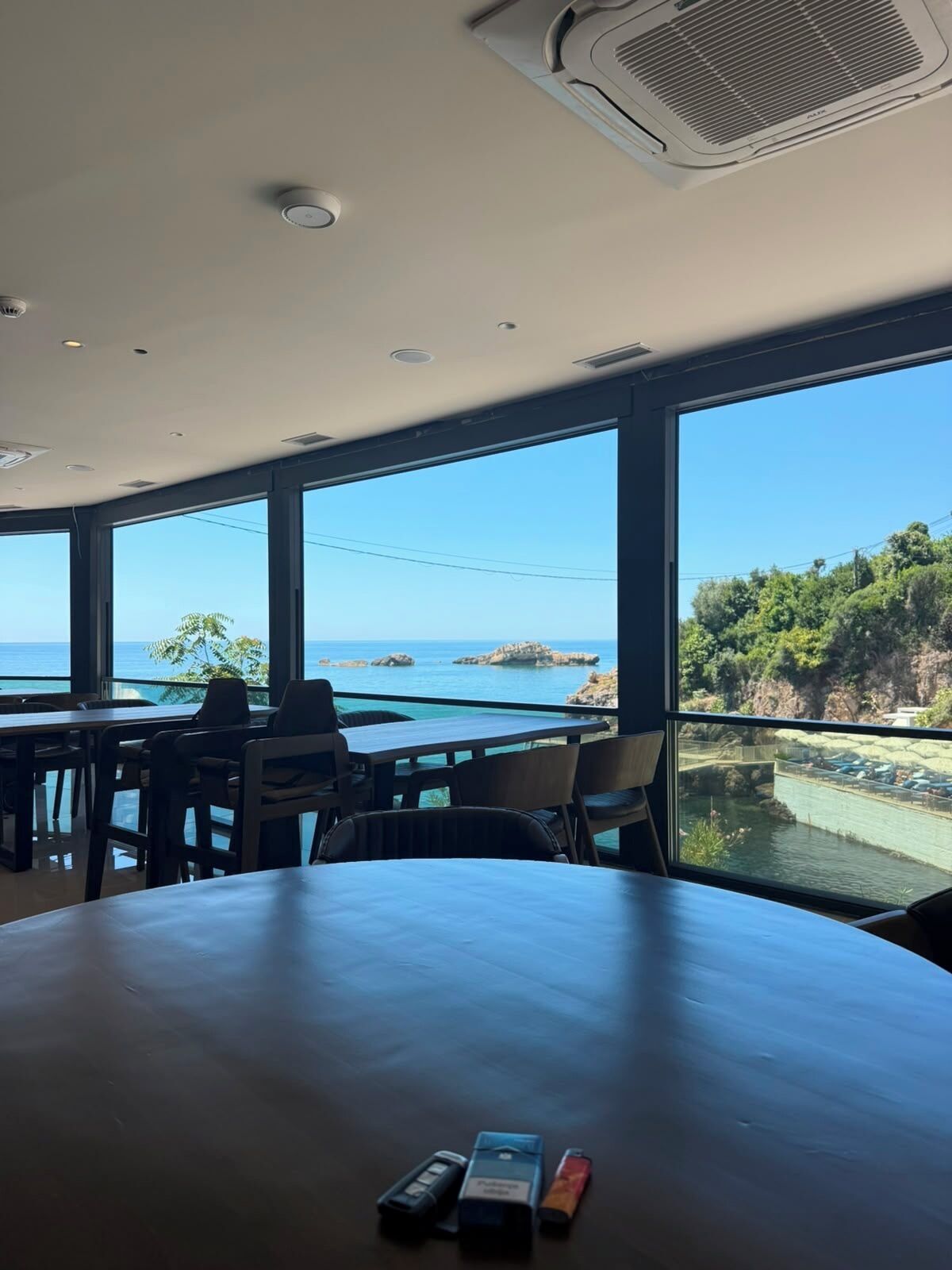 A dining area with a view of the sea, featuring tables and chairs, and a ceiling with an air conditioning unit.