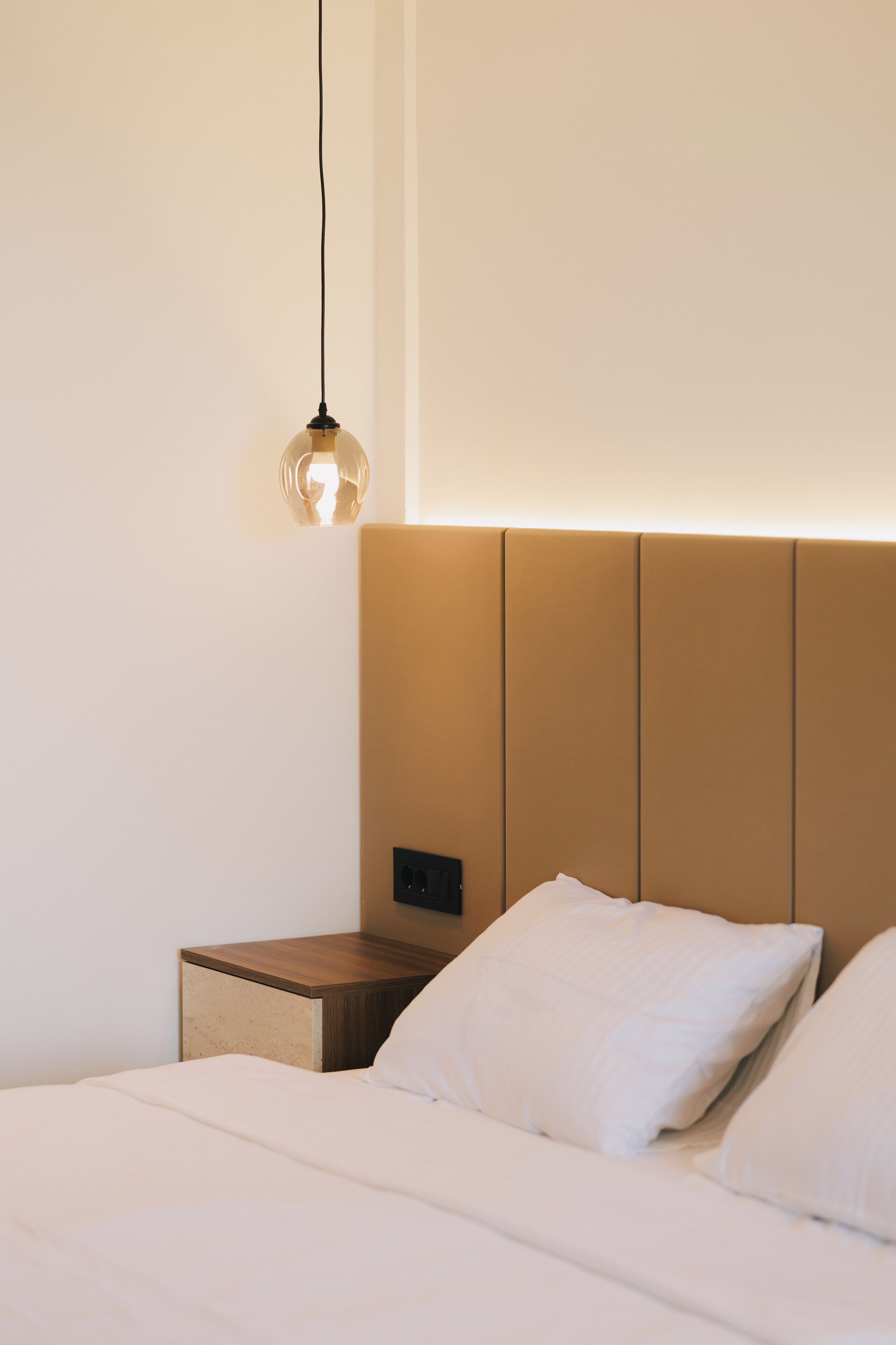 Une chambre d’hôtel au design minimaliste, comprenant un lit, une table de chevet et un luminaire fixé au mur.