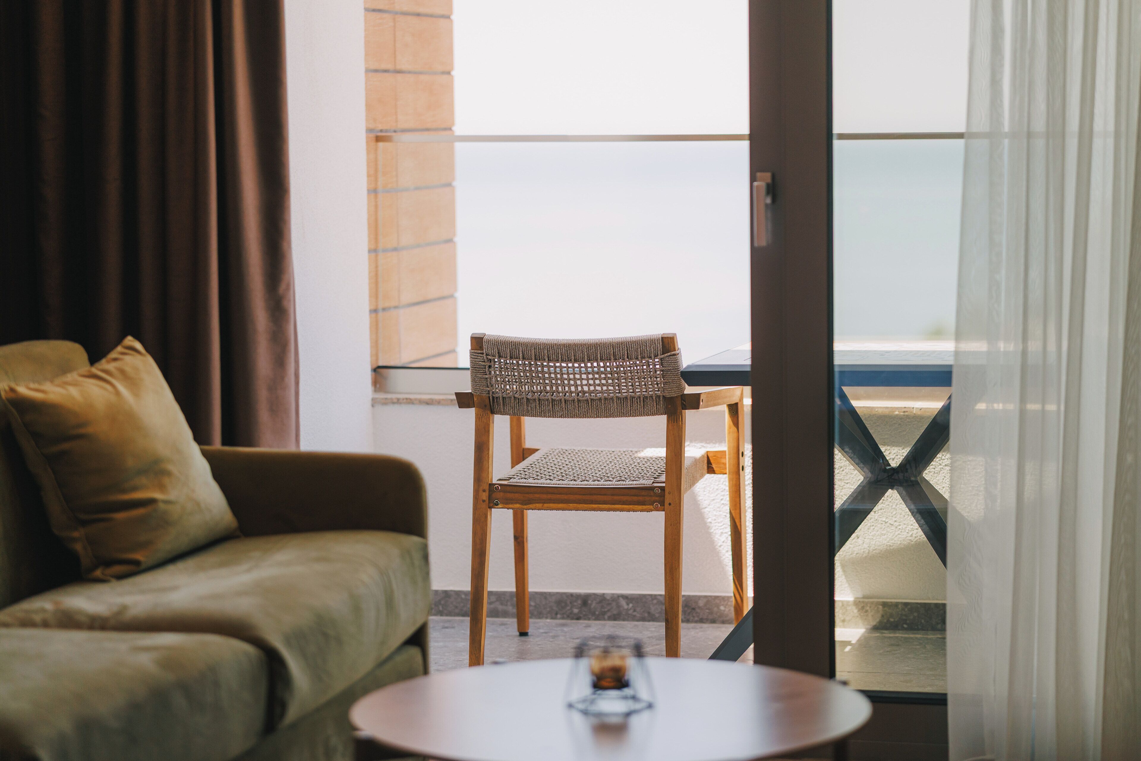Un balcon avec une chaise en osier et une petite table, un canapé et une vue sur la mer.