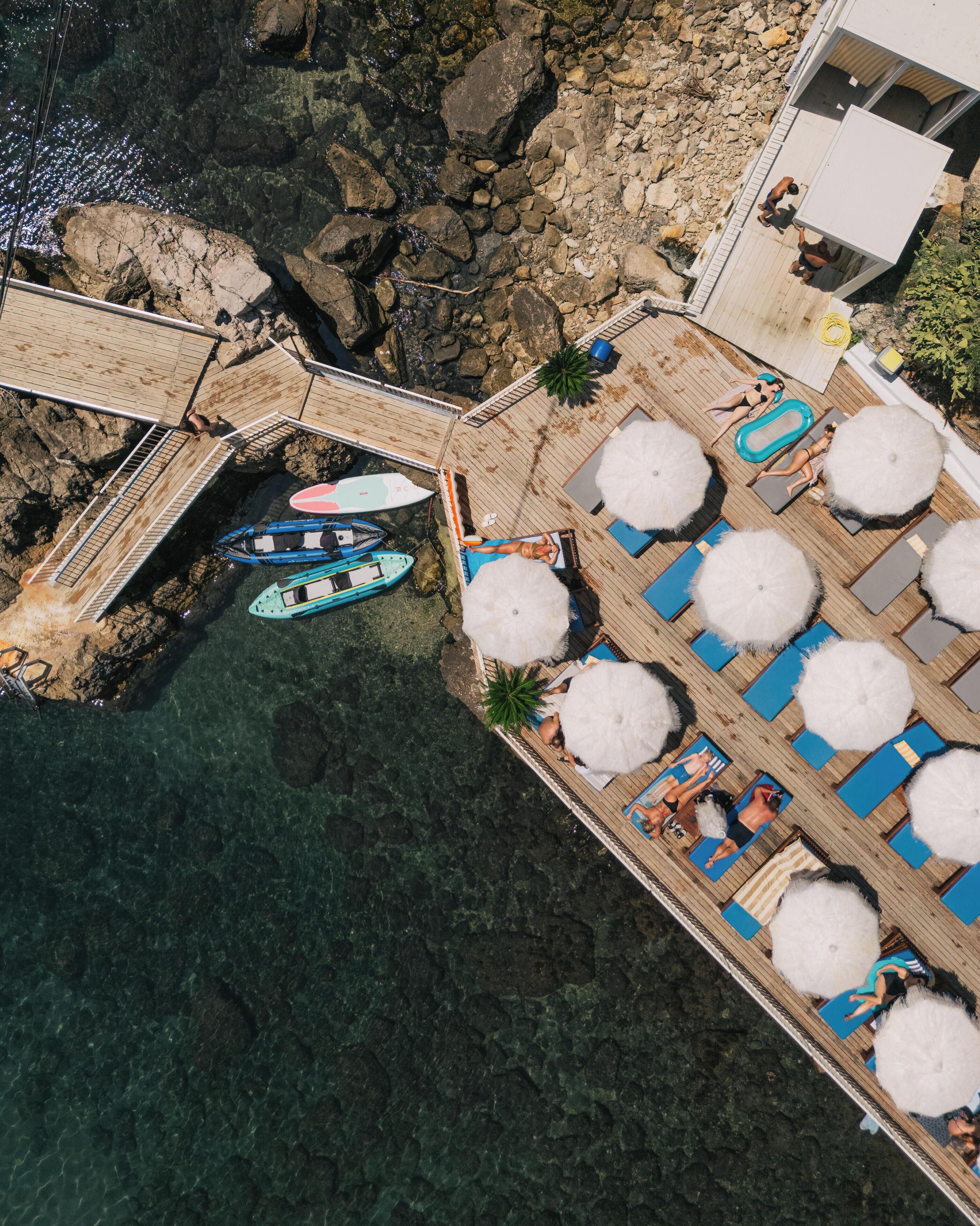 A wooden deck with a pool, lounge chairs, and a small boat docked.