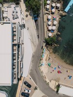 Vista aérea de una zona costera con una carretera, coches aparcados y una playa con sombrillas.
