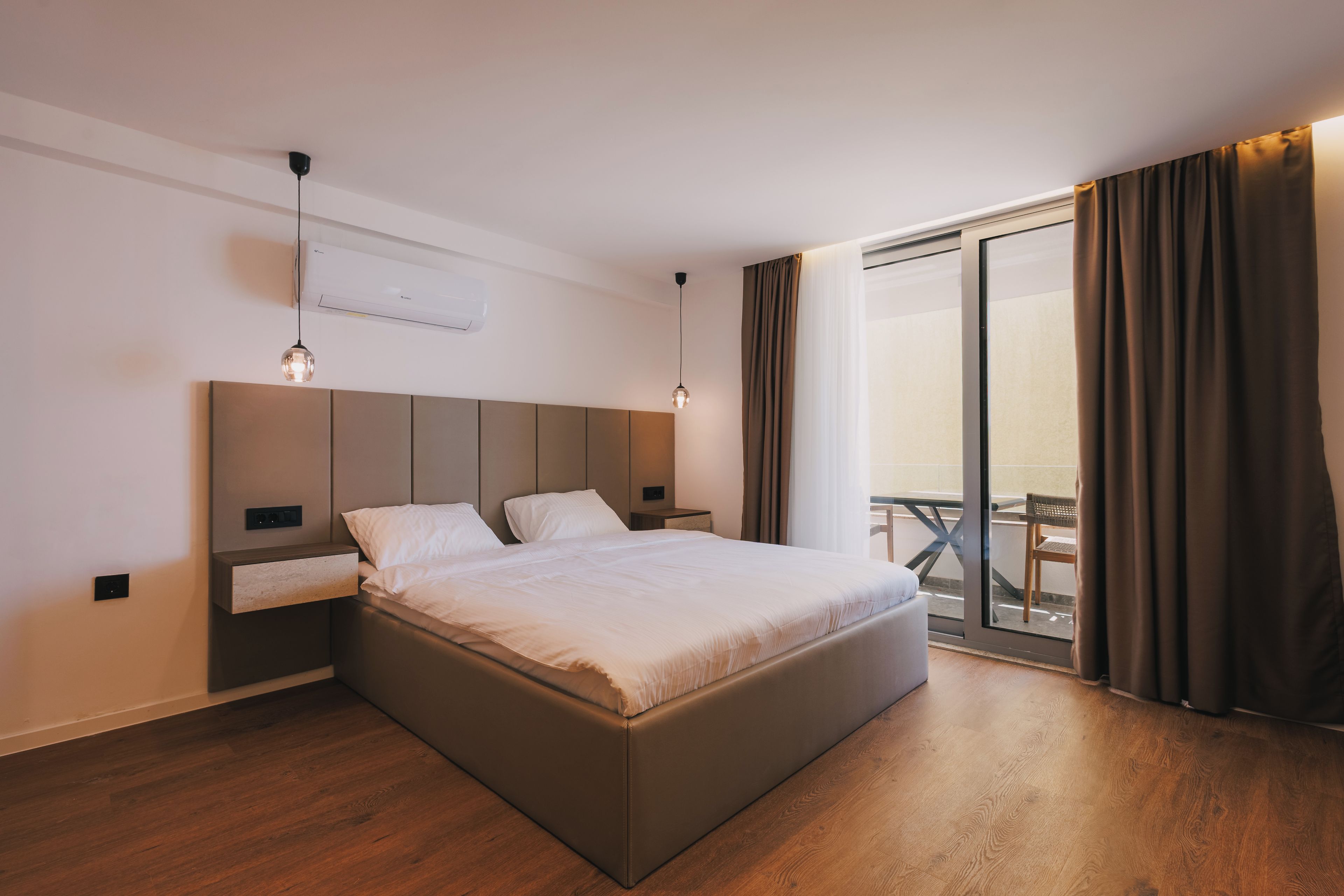 A modern hotel room with a large bed, bedside tables, a built-in TV, and a balcony with curtains.