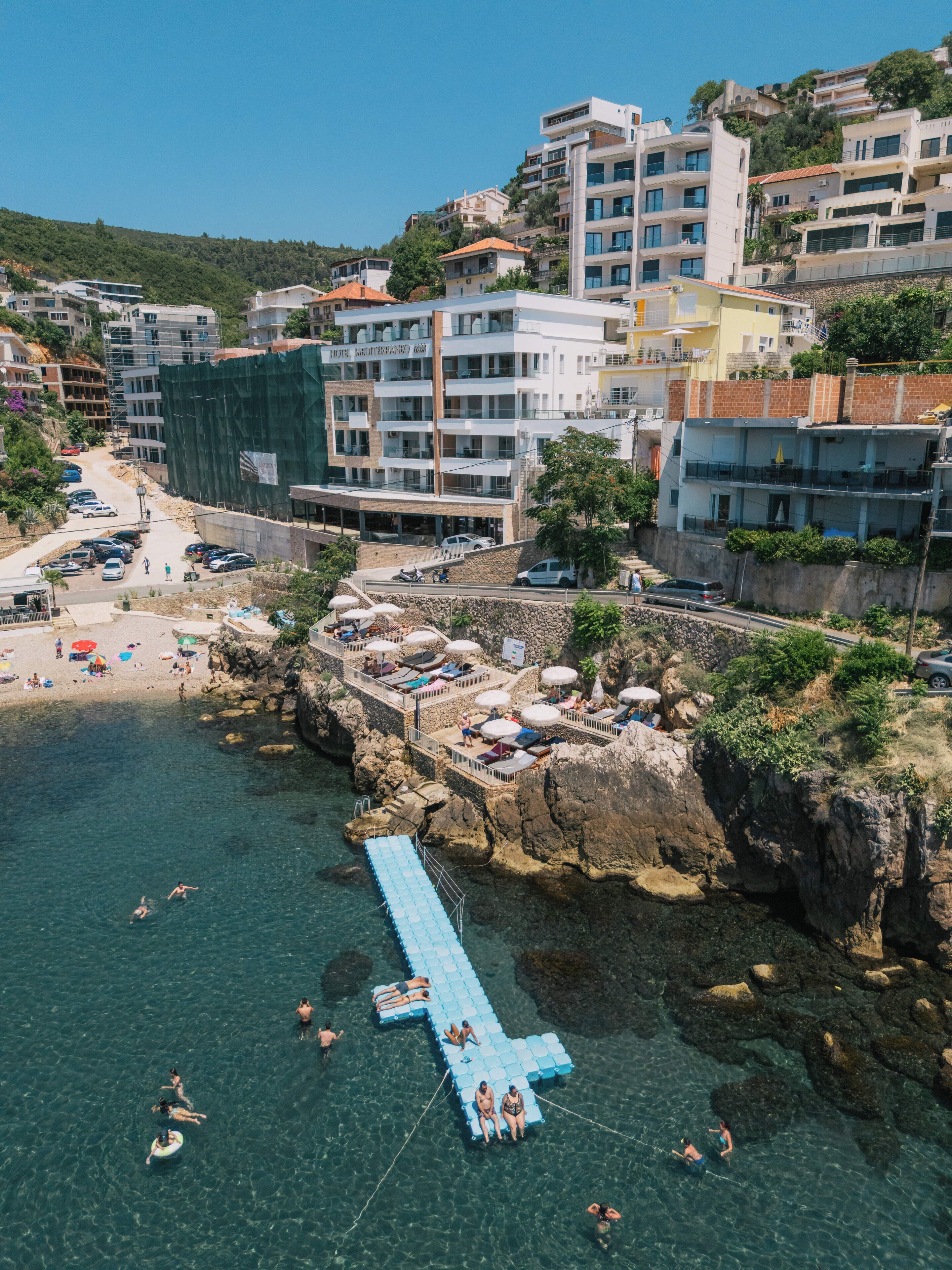 Un hotel costero con varios pisos, una zona de playa con sombrillas y un litoral rocoso.