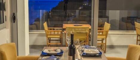 A dining area with a table set for two, a bottle of wine, and a view of the sea through large windows.