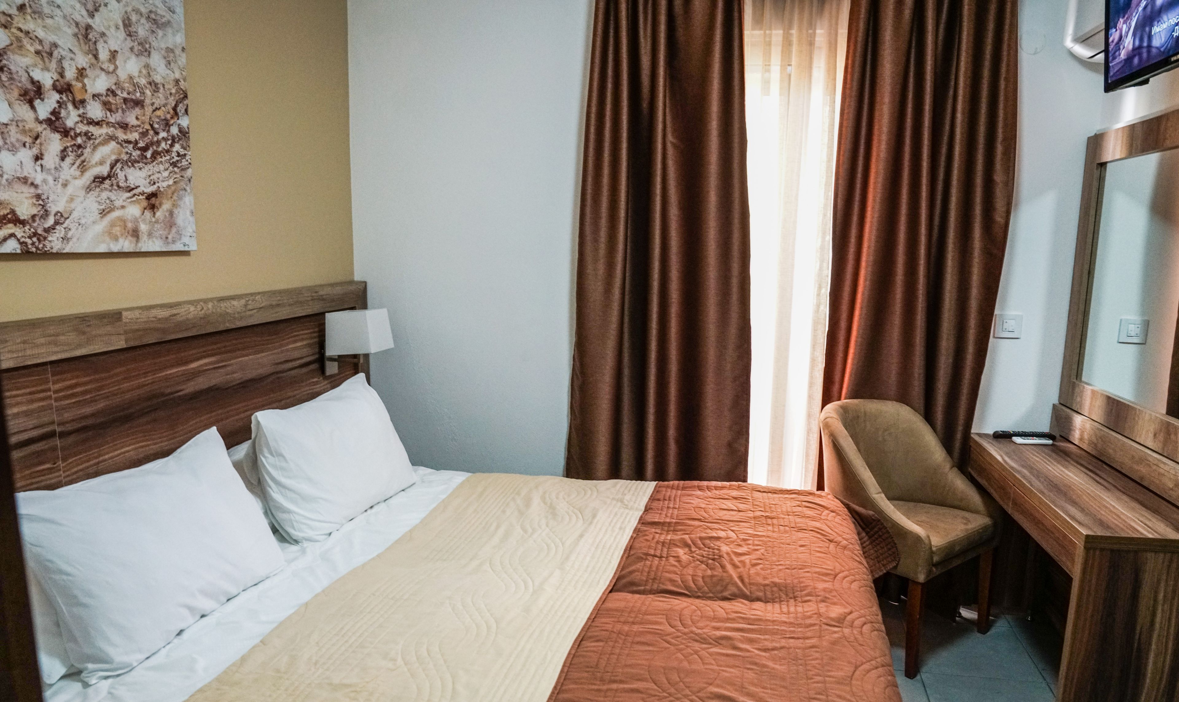 A hotel room with a bed, a desk, a chair, a TV, and curtains.