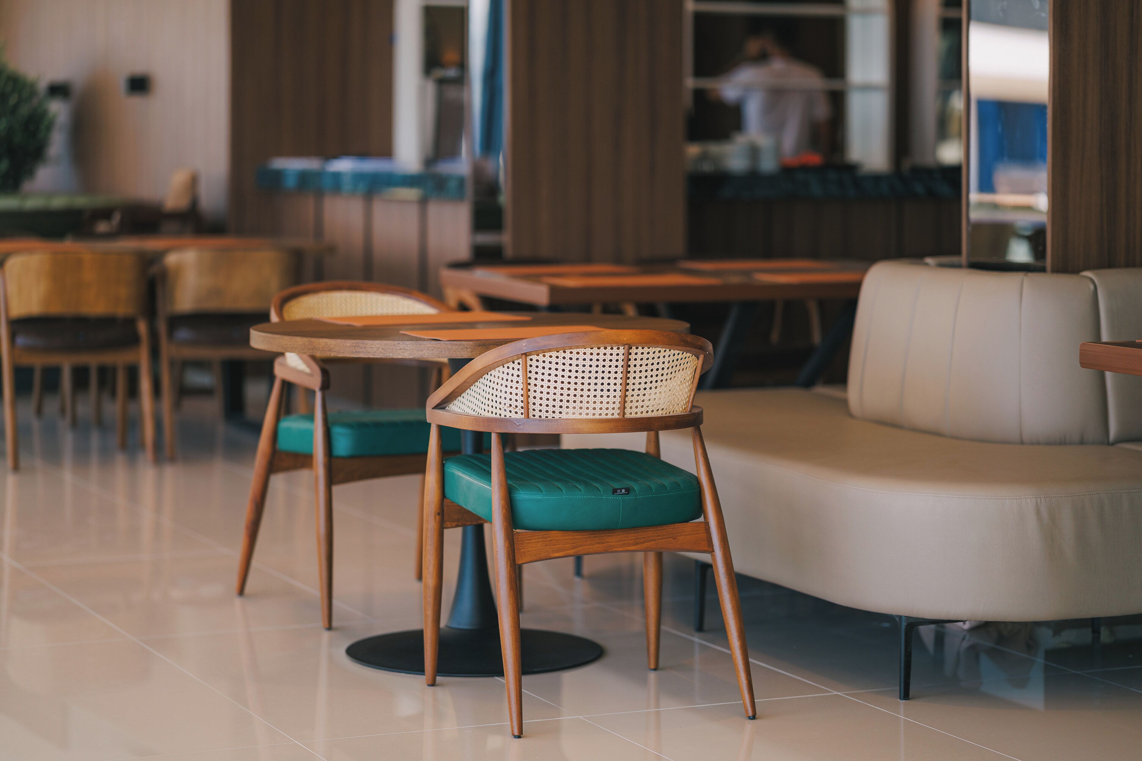 A modern cafe interior with wooden chairs, a cushioned sofa, and a tiled floor.