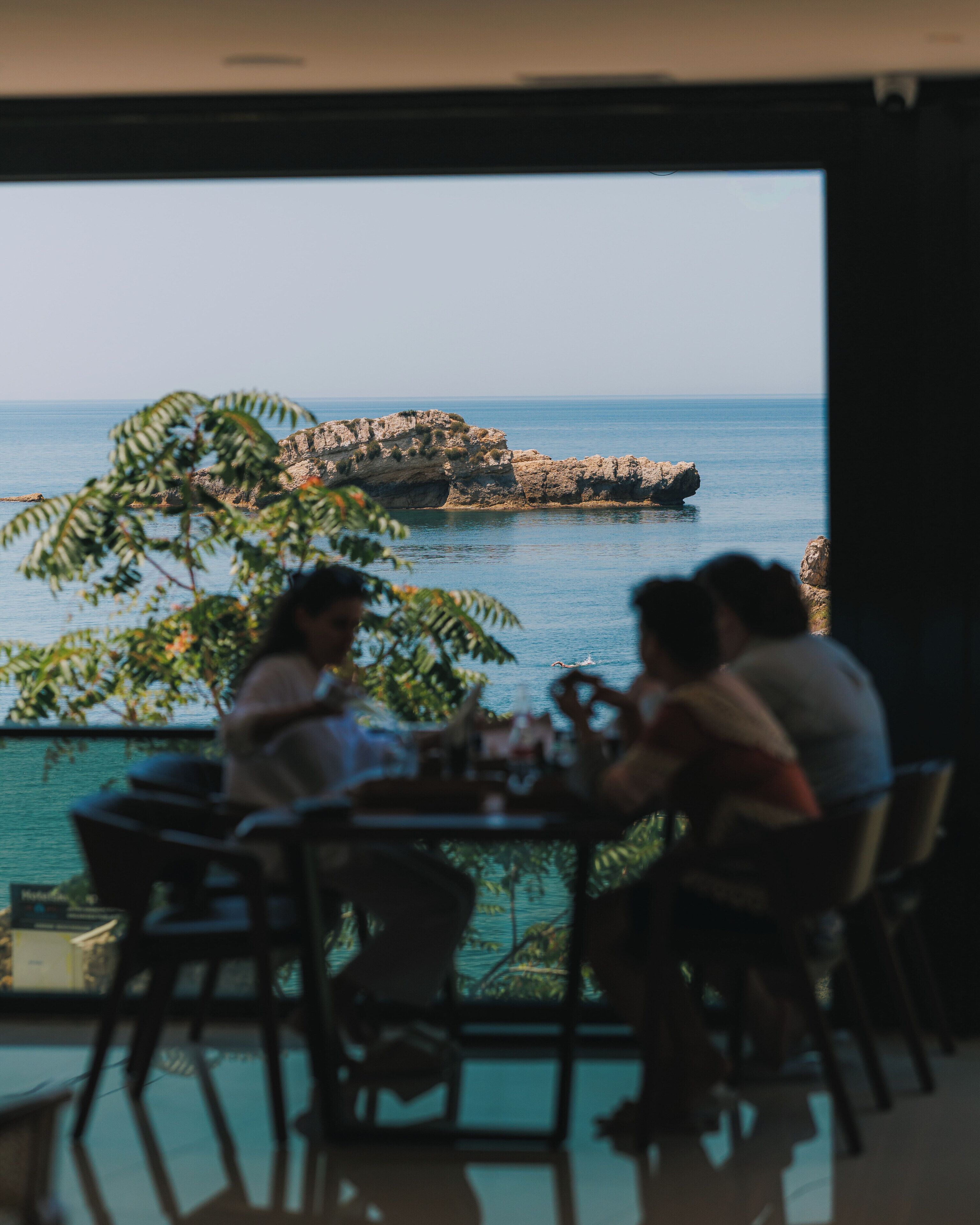 A dining area with a view of the sea and rocky outcrops.