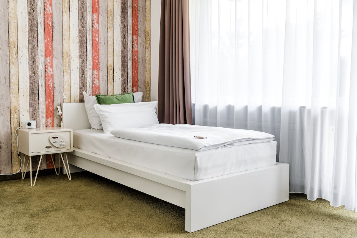 A modern bedroom with a white bed, a bedside table with a radio, and a wall with vertical wooden panels.