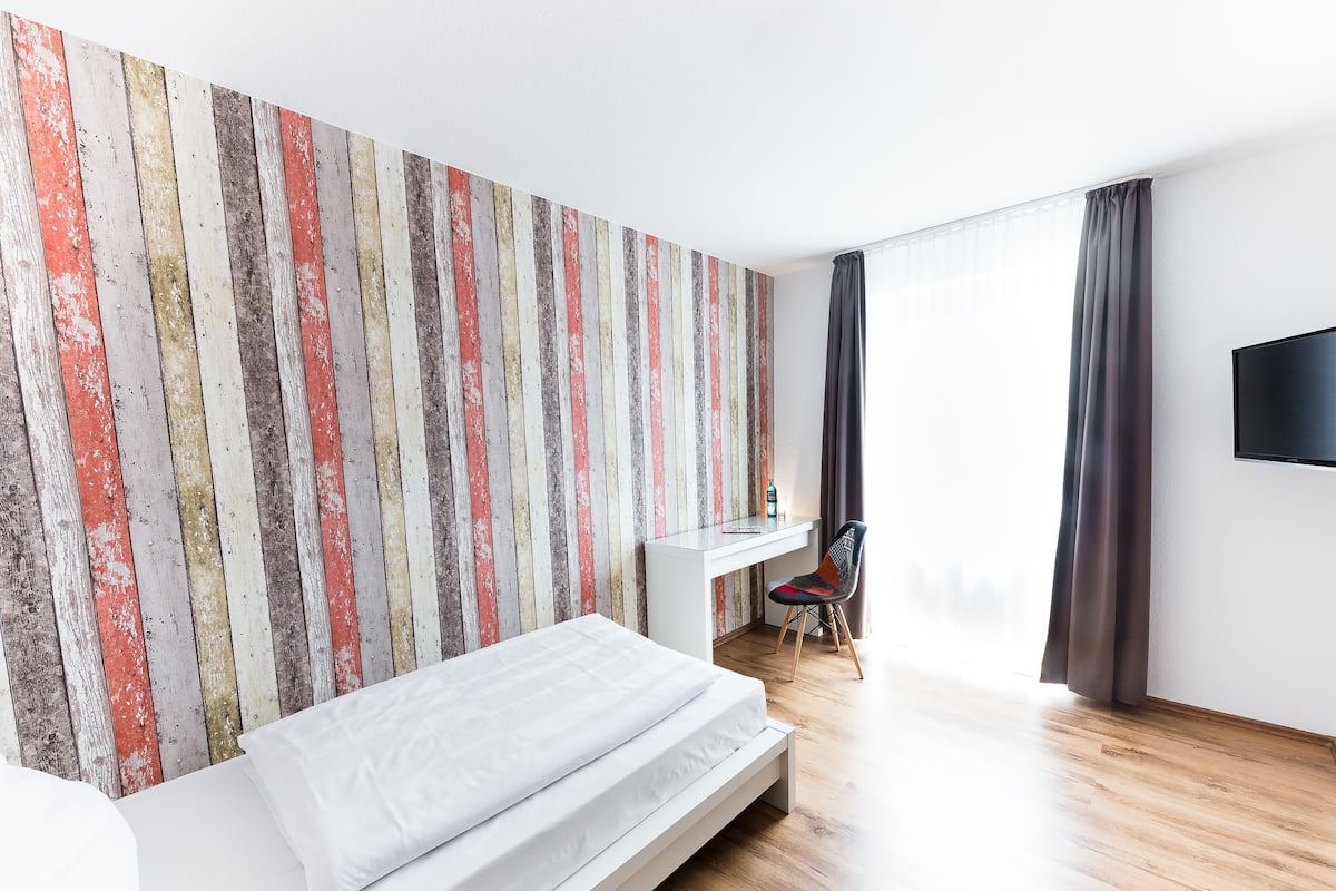 A modern hotel room with a bed, a desk, and a TV.