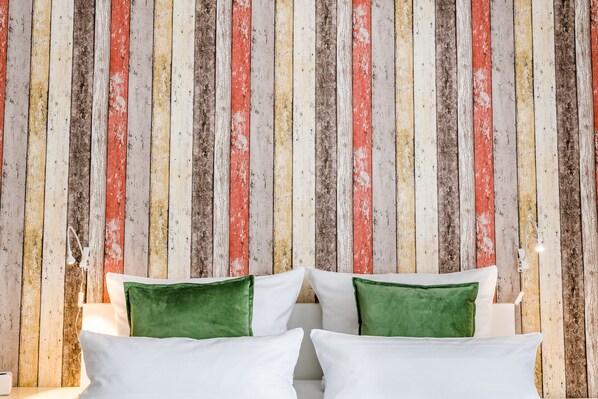 Un lit avec des oreillers blancs et verts, adossé à un mur en bois composé de planches verticales de différentes couleurs.