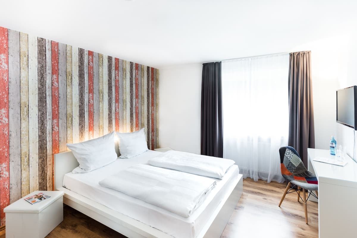 A modern hotel room with a large bed, a desk, and a chair.