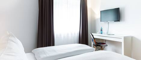 A hotel room with a bed, a desk with a computer, and a TV.