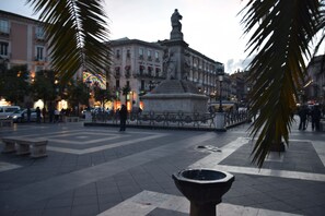 Una plaza pública con una fuente central, rodeada de palmeras y edificios con balcones.