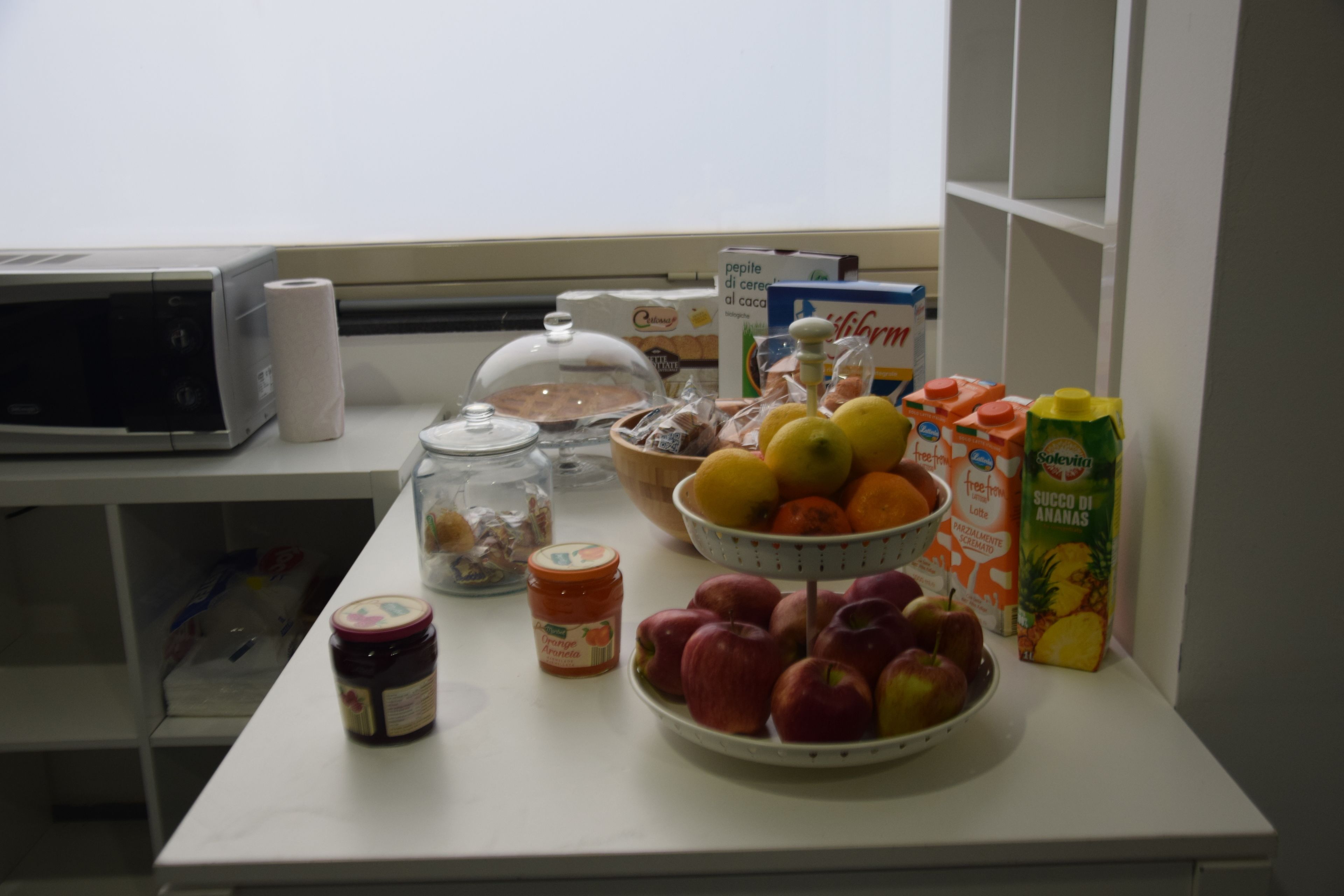 A kitchen counter with a microwave, jars, a bowl of fruit, and a carton of juice.