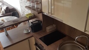 A modern kitchen with white cabinets, a stainless steel sink, a built-in oven, and a countertop with a coffee maker and jars. - Apartment Panorama Negotin (Negotin)