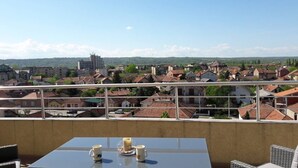 A balcony with a table and chairs, overlooking a town with red-roofed houses and a distant hill. - Apartment Panorama Negotin (Negotin)