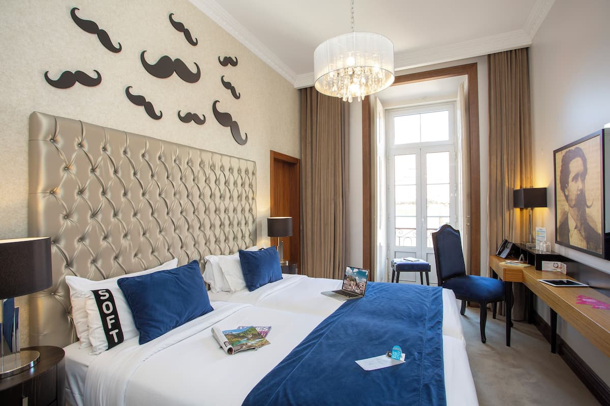 A hotel room with a tufted headboard, a bed with blue and white bedding, a desk with a laptop, and a chandelier.
