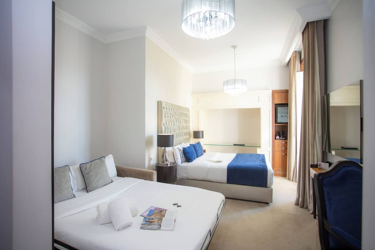 A hotel room with two beds, a desk, a chair, a mirror, a chandelier, and a wardrobe.
