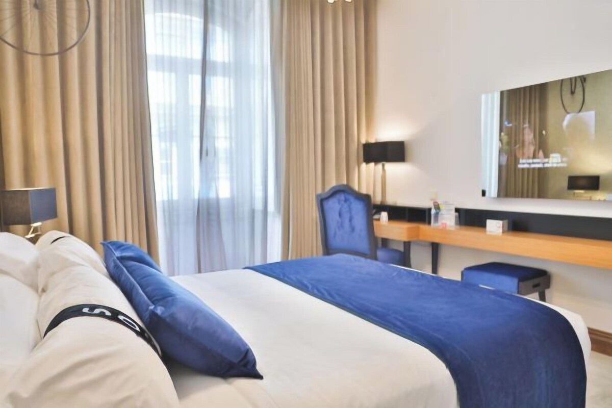 A hotel room with a bed, a desk, a chair, and a large mirror.