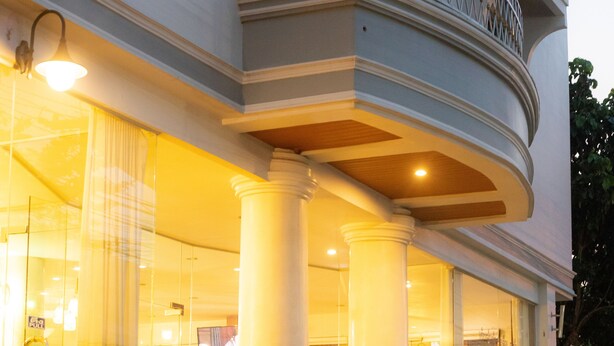 Un hotel con balcón, amplias columnas y una entrada bien iluminada.