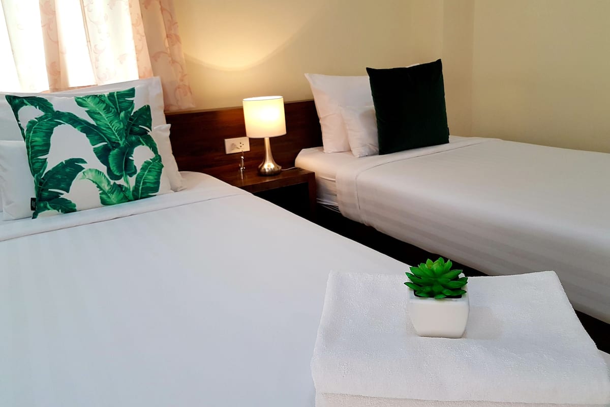 A hotel room with two beds, a nightstand with a lamp, and a small potted plant on a towel.