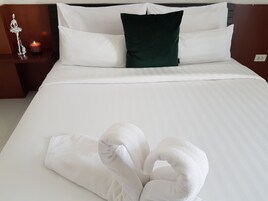 Una cama bien tendida con sábanas blancas, un cojín verde decorativo y una mesita de noche con una vela encendida y una figurita plateada.