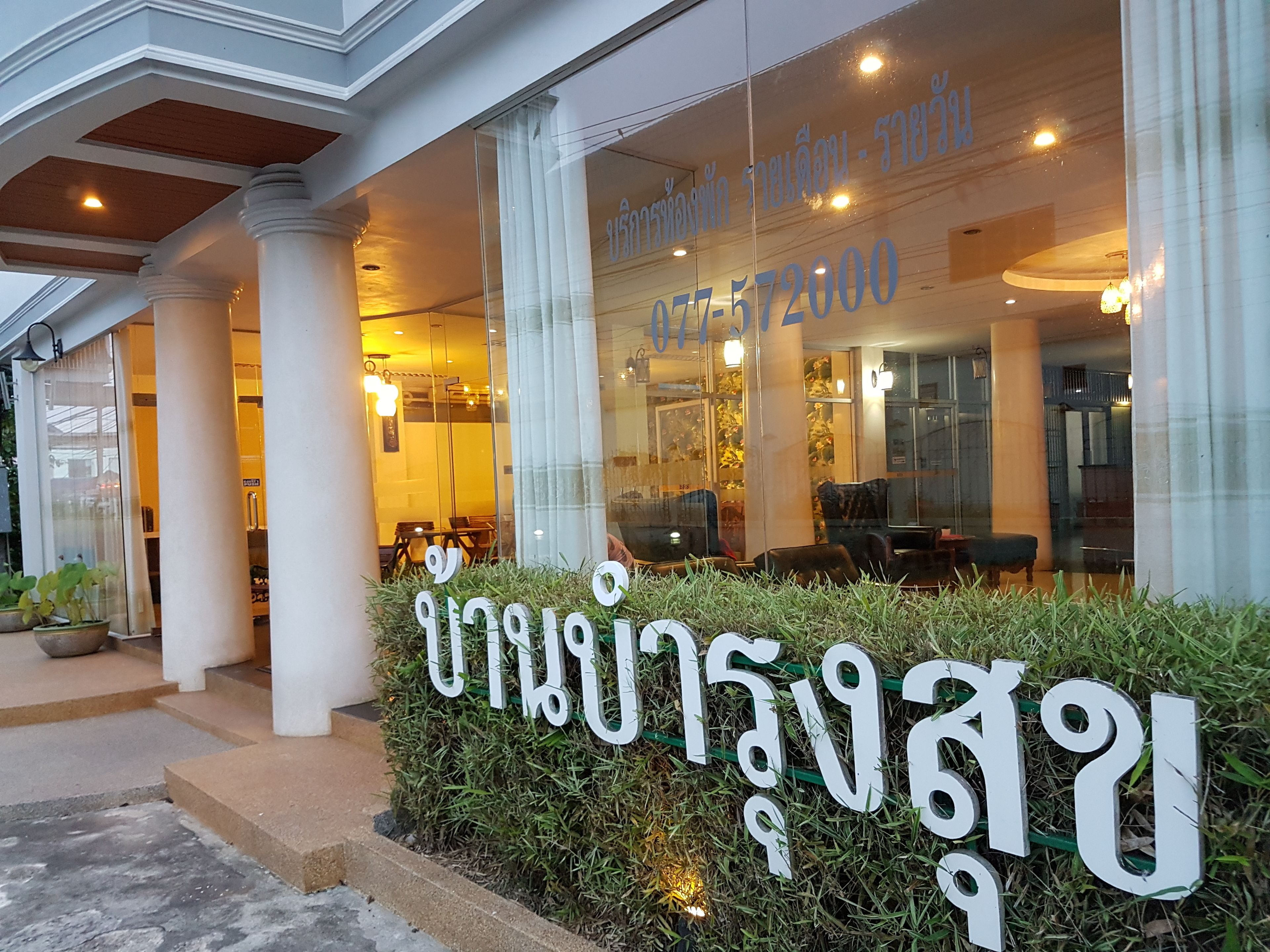 L’entrée d’un hôtel, avec une façade en verre, des colonnes et une enseigne en écriture thaïlandaise.