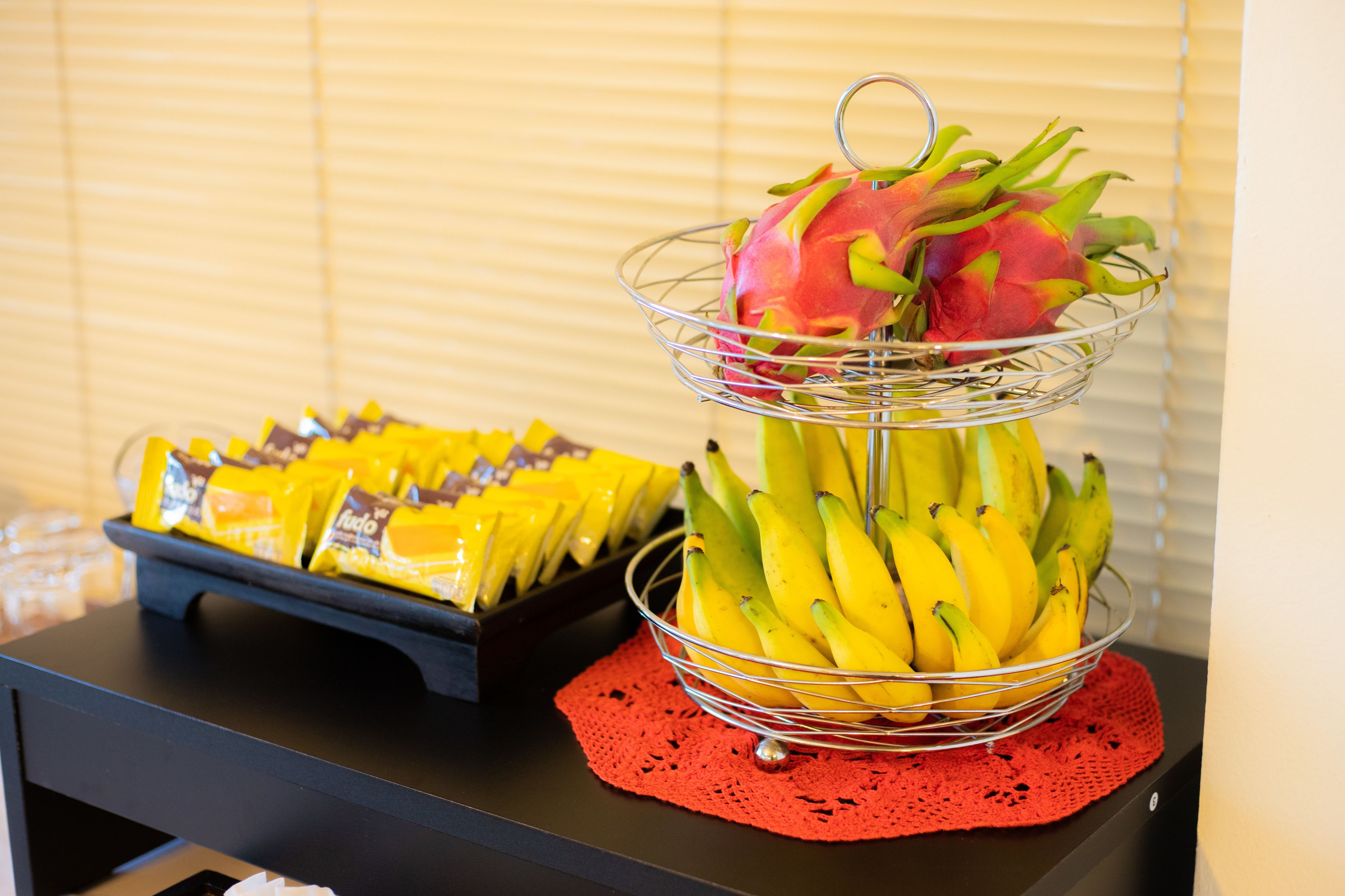 A table with a fruit basket containing bananas and a dragon fruit, and a tray of packaged snacks.