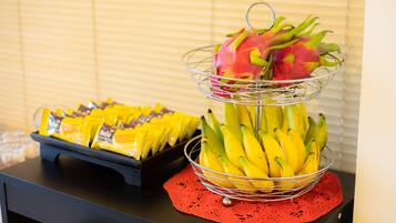 A table with a fruit basket containing bananas and a dragon fruit, and a tray of packaged snacks.
