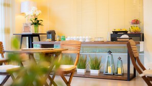 Un espacio interior bien iluminado con zona de comedor, estación de café y plantas decorativas.