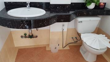 A bathroom with a white sink, black marble countertop, white toilet, and beige tiled floor.