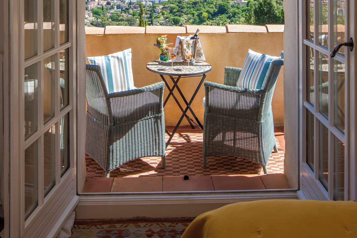 Ein offener Balkon mit Korbstühlen, einem kleinen Tisch mit Getränken und Blick auf die Stadt.