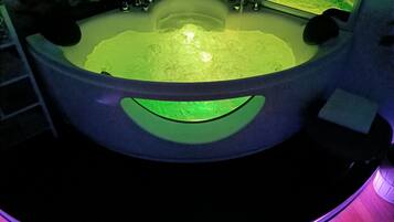 Une baignoire avec un éclairage vert en dessous, un robinet et un miroir au-dessus de la baignoire.