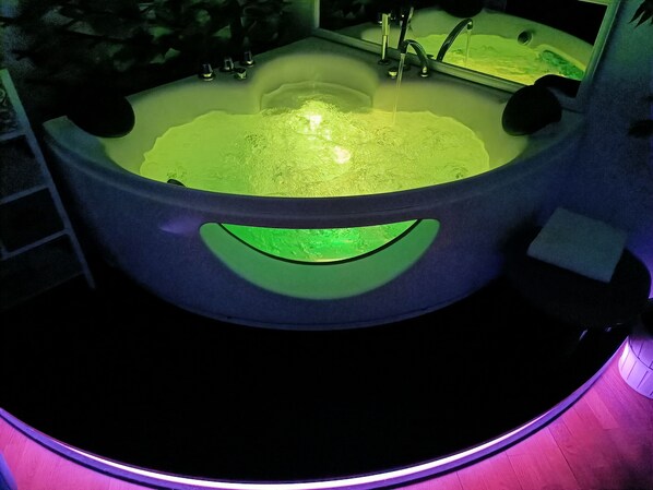 A bathtub with a green light underneath, a faucet, and a mirror above the tub.