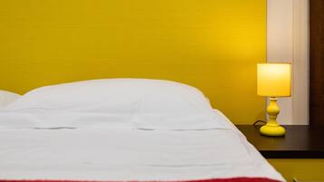 Un letto con biancheria bianca e una coperta rossa, una lampada gialla su un comodino e una parete gialla.