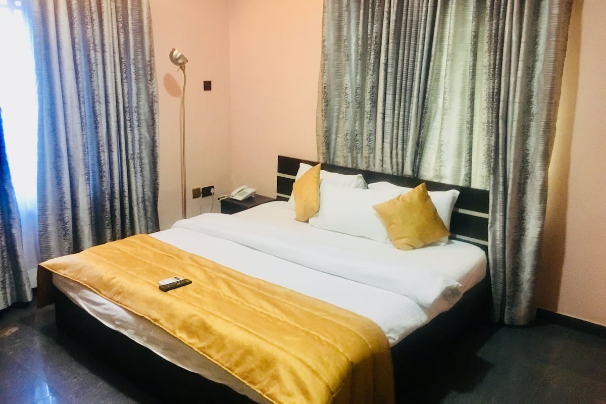 A hotel room with a bed, curtains, a bedside lamp, and a phone on a nightstand.