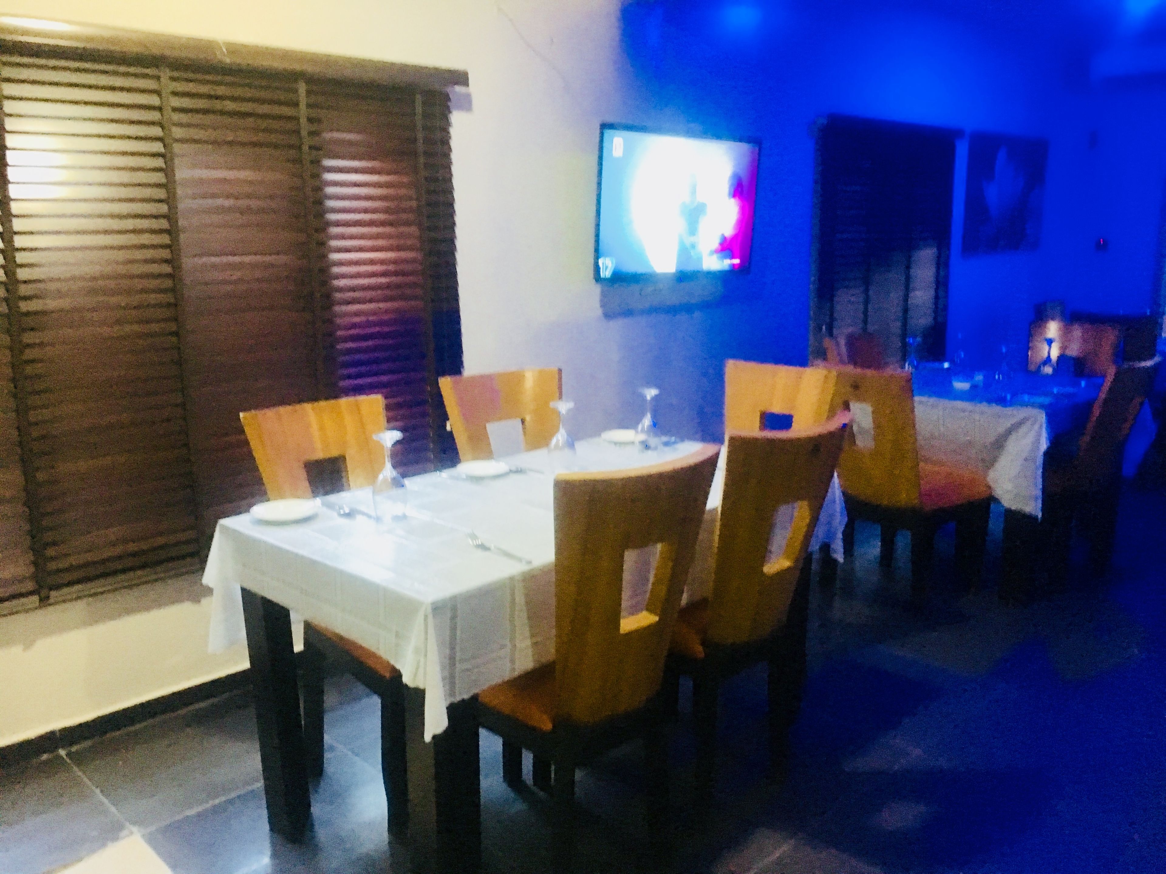 A dining area with a white table set for four, wooden chairs, and a television mounted on the wall.