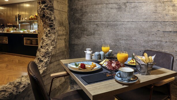 Een ontbijtsetting met een stenen zuil, een houten tafel en uitzicht op een keuken.
