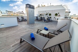 Una terraza en la azotea con sillones, una mesa y un muro decorativo.