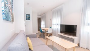 Een moderne woonkamer met een grijze bank, een houten salontafel, een televisie en een eethoek met blauwe stoelen.