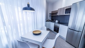 Een moderne keuken met witte kastjes, een roestvrijstalen koelkast, en een eethoek met een witte tafel en stoelen.