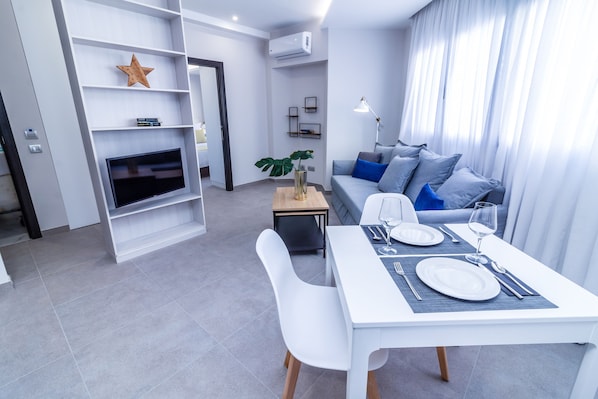 Una sala de estar moderna con comedor, muebles blancos, un televisor de pantalla plana y un adorno con forma de estrella en la estantería.