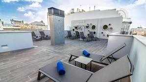 Een terras op het dak met lounge fauteuils, een tafel en een decoratieve muur.