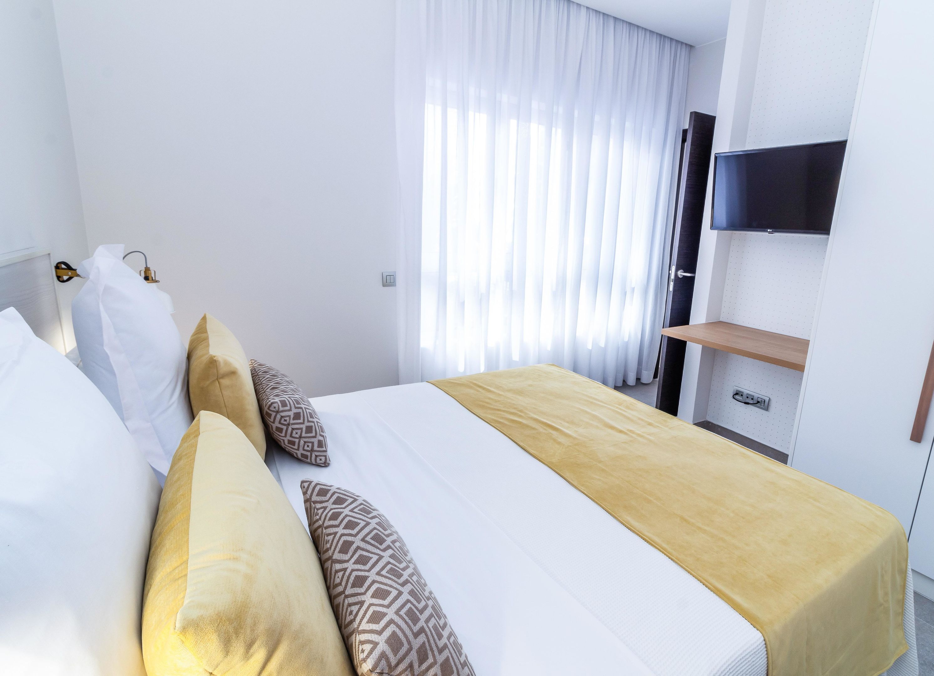 Quarto de hotel com cama, almofadas, televisão e prateleira.