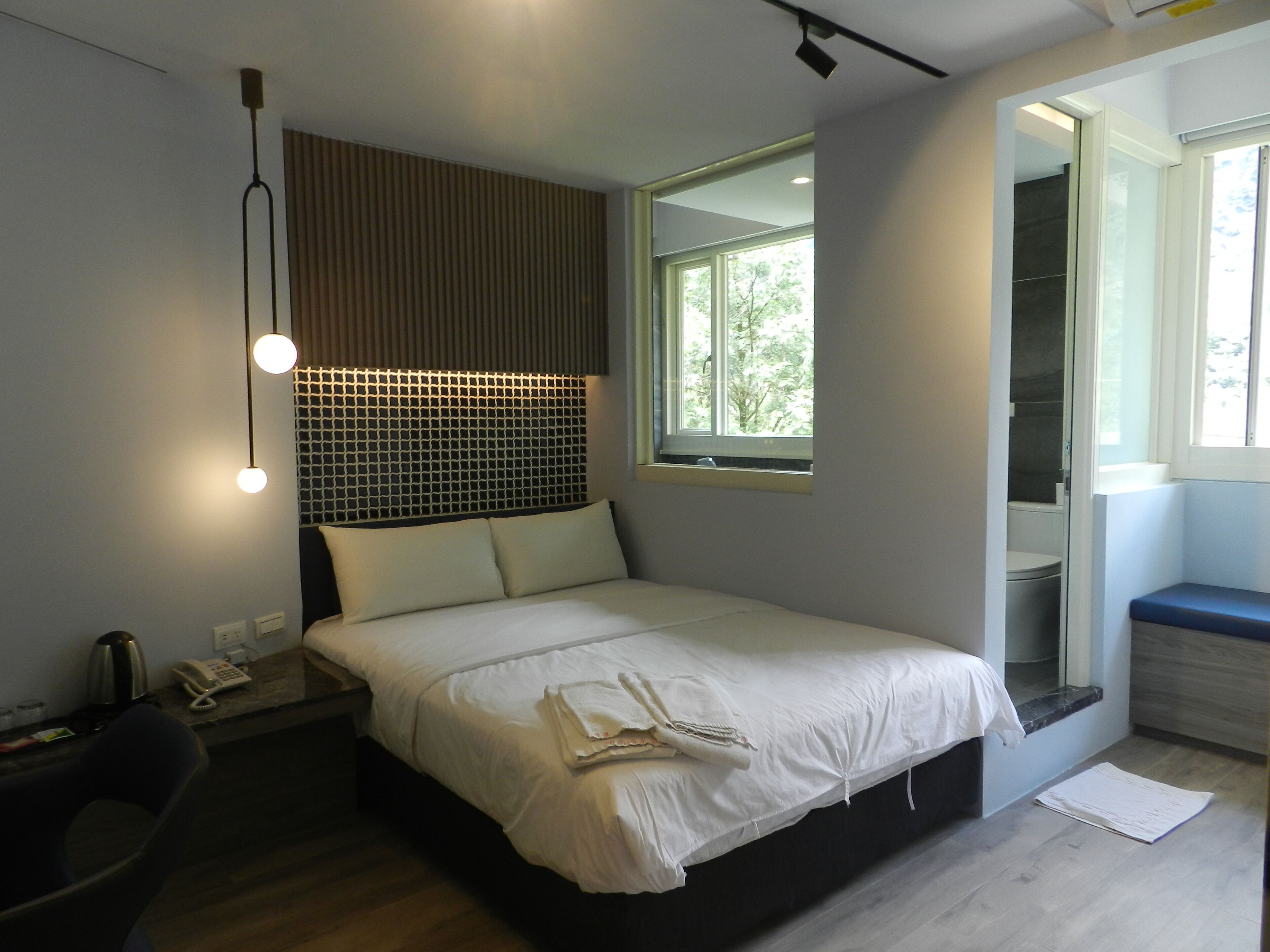 Una habitación de hotel moderna con una cama grande, una mesita de noche y una ventana con vistas a árboles.