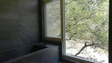 A bathroom with a bathtub, a window, and a view of trees.