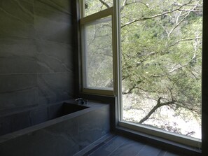 A bathroom with a bathtub, a window, and a view of trees.