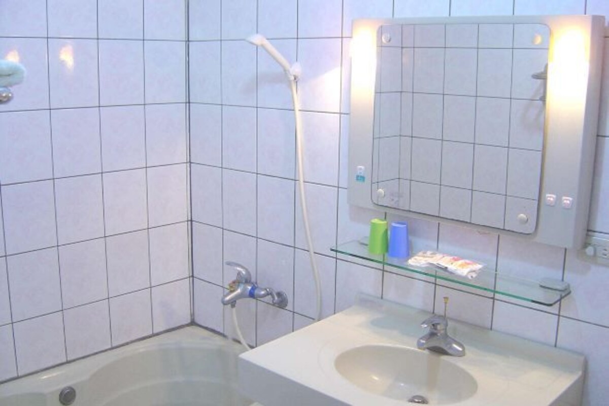 A bathroom with a bathtub, a sink, a glass shelf with toiletries, and a mirror.