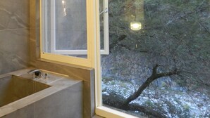 Ein Badezimmer mit einer Badewanne, einem Fenster und Blick auf Bäume.